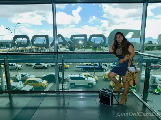 Mujer sentada junto a un parlante portátil frente a ventanales con vista a un estacionamiento