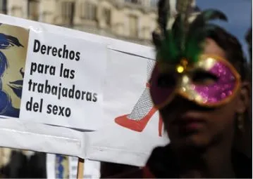 Manifestante con antifaz de carnaval junto a una pancarta que dice «Derechos para las trabajadoras del sexo»